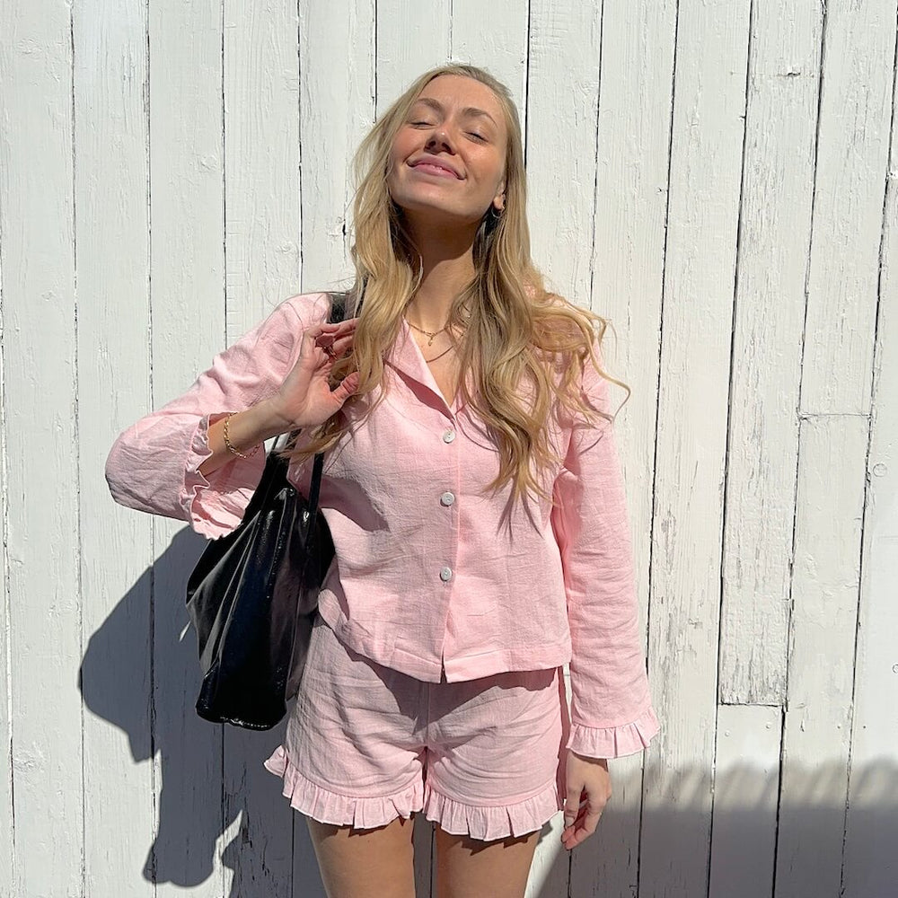Woman in pink pajamas and black bag smiling.