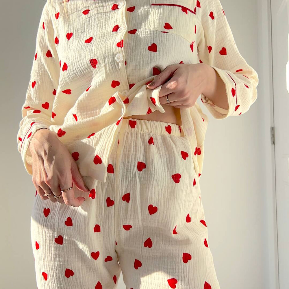 Woman in cream pajamas with red heart print.