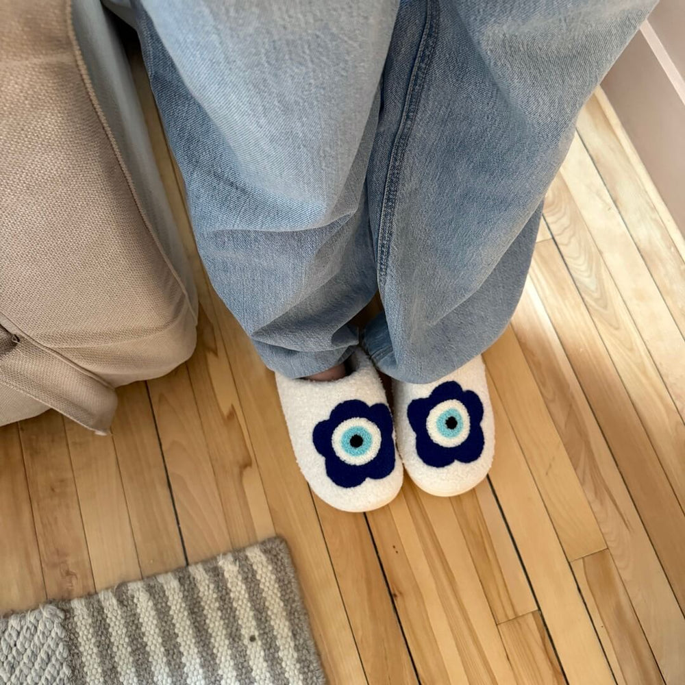 Person wearing jeans and flower-eye slippers on wooden floor.