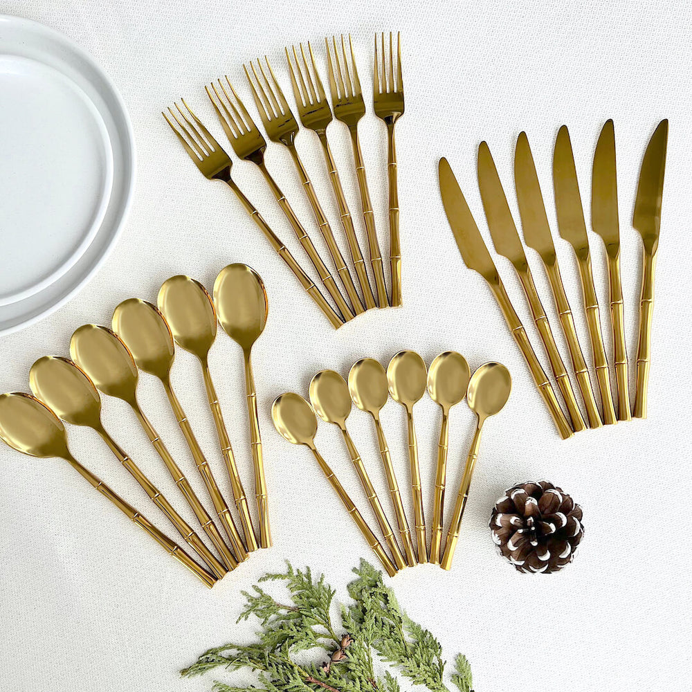 Gold flatware, plate, and pinecone on a white surface.