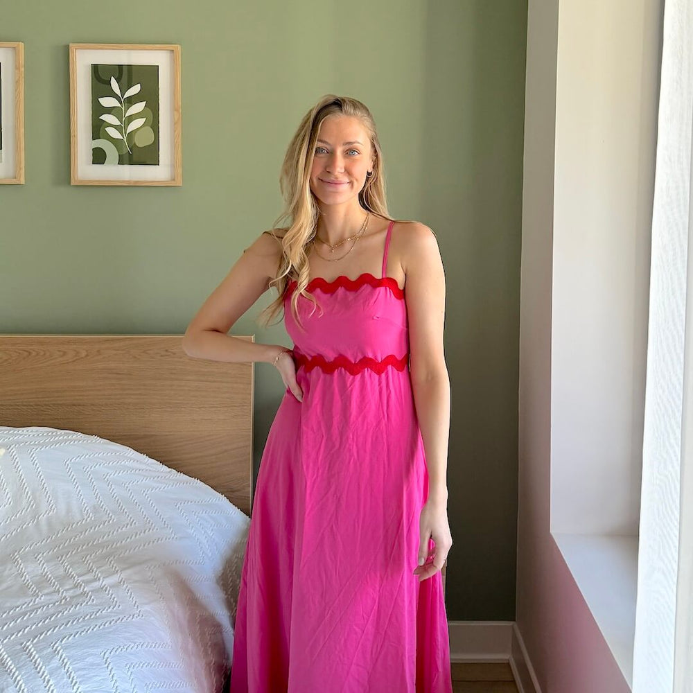 Woman in pink dress in front of a bed.