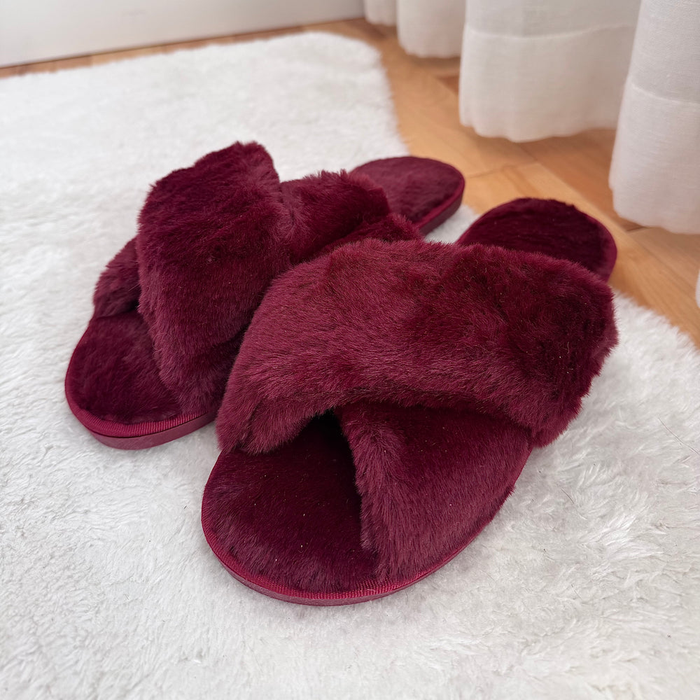 Burgundy fuzzy slippers on white rug.